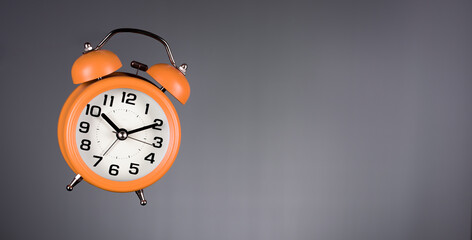 Flying orange alarm clock on grey background