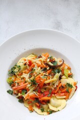 white plate with round ravioli and lots of different vegetables, thinly sliced vegetables and Italian dumplings, egg pasta ravioli, Italian dumplings, mixed vegetables