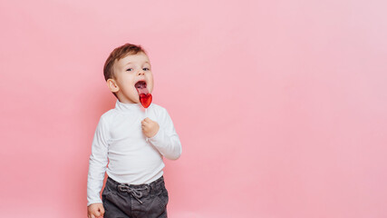 studio portrait of a little boy with a heart-shaped lollipop in his hand.