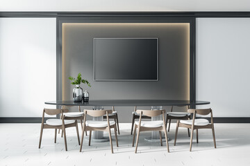 Black blank screen in the center of dark wall panel with lights around and big table with modern wooden chairs on ceramic floor tiles. Mock up