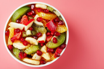 Fruit salad in a cup on a pink background.