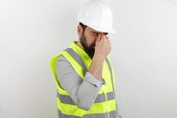 Bearded man architect wearing safety helmet and reflective jacket tired rubbing nose and eyes...