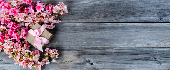 Top view of a gift box with pink cherry blossoms on weathered wooden planks for Mothers day love holiday