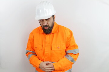 Bearded man wearing hardhat and reflecting jacket  touching belly with hand with painful expression, intestinal discomfort.