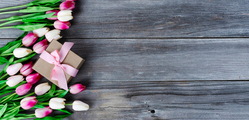 Top view of a gift box with pink tulips on weathered wooden planks for Mothers day love holiday