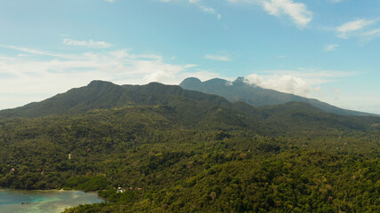 Tropical landscape: Mountains with forest, against blue sea with blue sky with clouds, top view, Camiguin, Philippines. Mountain landscape on tropical island with mountain peaks covered with forest