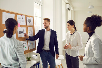 Business team analyzes sales graphs and charts, develops a new strategy, discussing work issues. Young project manager makes a suggestion or points out a mistake at the meeting. Concept of teamwork.