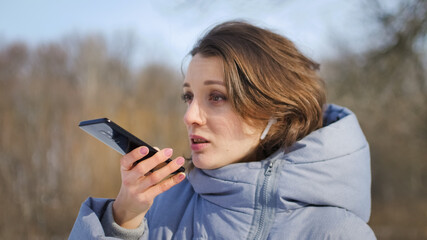 Young girl in blue coat is using her smartphone to send a voice message to a new social network...