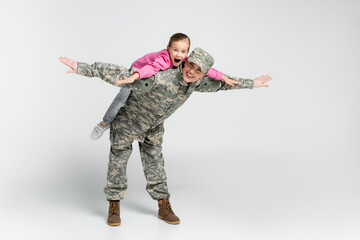 Amazed girl piggybacking on mother in camouflage on grey background