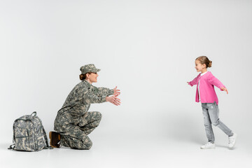 Soldier in uniform outstretching hands near daughter on grey background
