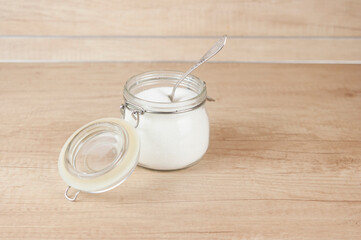 Opened glass jar with sugar. Standing on wooden table