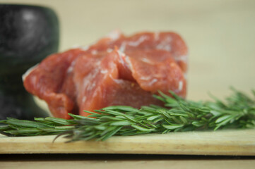 A large piece of pork and two sprigs of rosemary on a wooden table. Ingredients for cooking meat dishes.