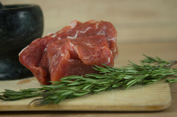A large piece of pork and two sprigs of rosemary on a wooden table. Ingredients for cooking meat dishes.