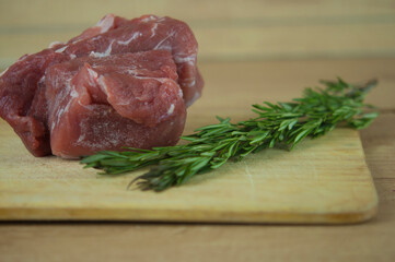 A large piece of pork and two sprigs of rosemary on a wooden table. Ingredients for cooking meat dishes.