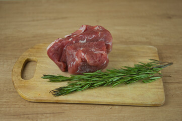 A large piece of pork and two sprigs of rosemary on a wooden table. Ingredients for cooking meat dishes.