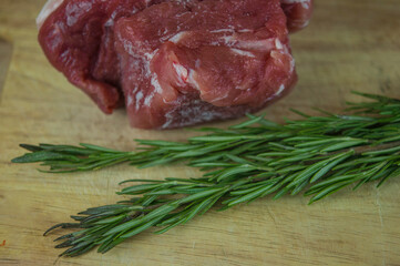 A large piece of pork and two sprigs of rosemary on a wooden table. Ingredients for cooking meat dishes.