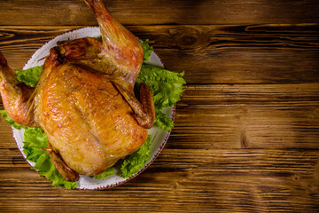 Plate with roasted whole chicken and lettuce leaves on a wooden table. Top view