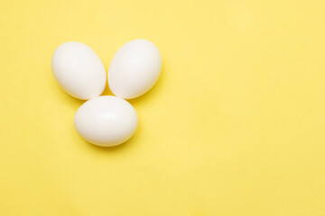 three white chicken eggs on a yellow background. Happy Easter