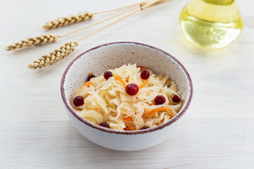 Sauerkraut with cranberries in a bowl on a background of vegetable oil and wheat. Russian traditional food.