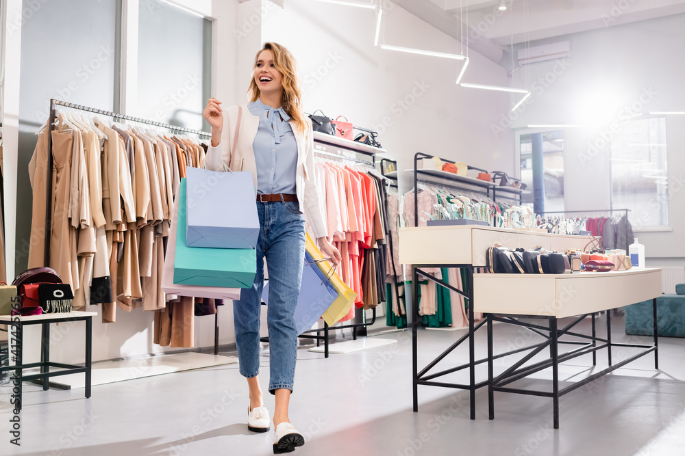 Wall mural Happy shopaholic walking with shopping bags in showroom