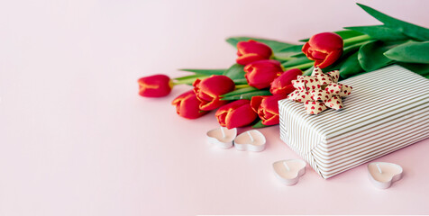Obraz na płótnie Canvas Bouquet of red tulips and gift wrapping box on a pink background. Banner, copy space for text.