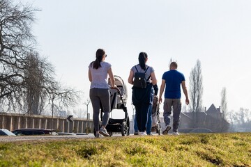 The first days of spring, people go for a walk on a sunny day, a girl with a baby carriage and in...