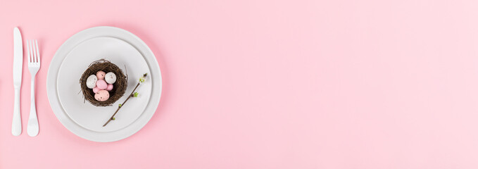 Easter holiday table setting on a pink paper background.Plates with colorful eggs. Easter holiday concept .Top view, copy space.Banner