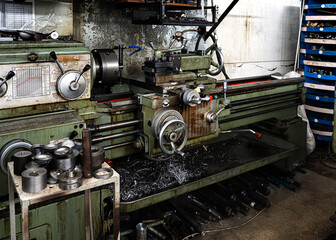 An old, in working condition, lathe stands in the production room surrounded by tools and tools. At the bottom, shavings from metal products.
