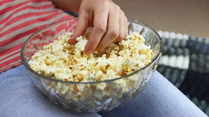 Girl eating popcorn at home in front of the TV, hand close-up
