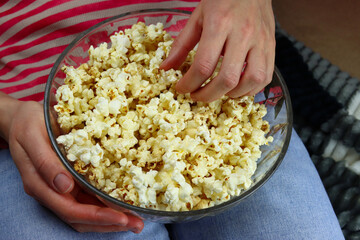 Girl eating popcorn at home in front of the TV, hand close-up
