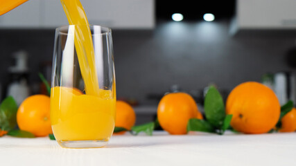 Orange juice pouring into glass on white table. Citrus juice splash