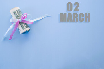 calendar date on blue background with rolled up dollar bills pinned by blue and pink ribbon with copy space. March 2 is the second day of the month