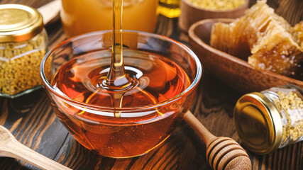 Honey in glass jar with honey dipper over wooden background