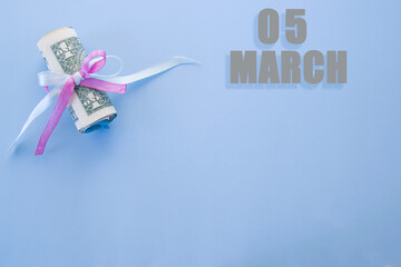 calendar date on blue background with rolled up dollar bills pinned by blue and pink ribbon with copy space. March 5 is the fifth day of the month