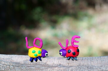 Obraz premium Two ladybugs made of plasticine in the forest on a colored background. They carry letters. The inscription love.