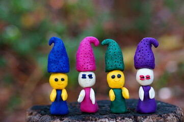 Figures of four fairy-tale dwarfs made of plasticine in the forest on a colored background.