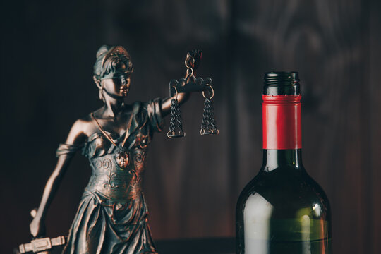 Bottle of wine and lady of justice as a symbol of law close-up. Alcohol and crimes concept.