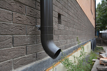 A close-up on a metal rain gutter downpipe, downspout of a roof gutter system and a foundation vent...