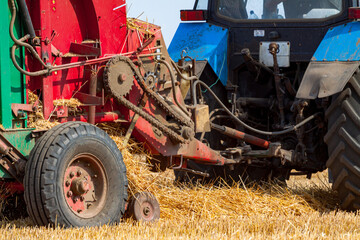 A tractor with a trailed bale making machine collects straw rolls in the field and makes round...