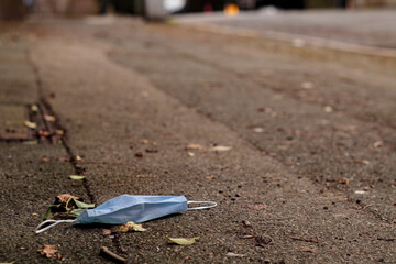 Single use face mask thrown on the asphalt sidewalk with blurred background.