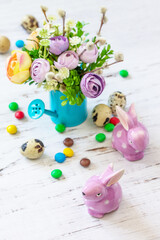Happy Easter background with spring flowers, easter eggs, sweets and easter bunny on a white wooden background.