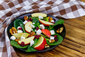 Autumn spinach salad with apple, feta cheese, walnut and dried cranberry on wooden table. Healthy vegetarian food