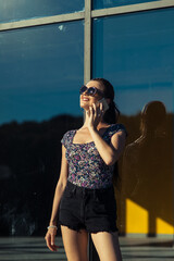 A smiling girl near the window is talking on the phone. A woman with a phone in her hands. Communication.