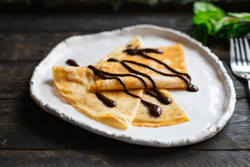crepes in a white plate thin pancakes pour chocolate syrup flat cake Shrovetide snack healthy meal top view copy space for text food background rustic
