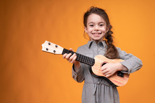 A cute girl in a dress holds a small guitar in her hands and plays it smiling