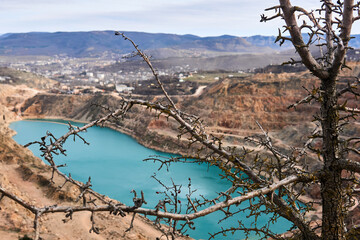 dry tree on the edge of a deep abandoned quarry with a blue lake at the bottom