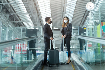 Caucasian business man travels with young asian woman on airport escalator. Keep wearing mask and...