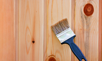 A wall made of wooden lining with knots is varnished with a brush