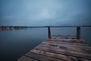 Wooden pier on the blue lake in the morning with a cloudy sky