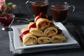 Homemade pancakes with curd filling and cherry sauce on a white plate on a dark background.